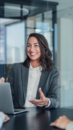 A imagem mostra três pessoas conversando no que parece ser uma reunião em uma empresa. A mulher em destaque está na frente de um notebook e gesticula para explicar o processo de como criar uma marca do zero.