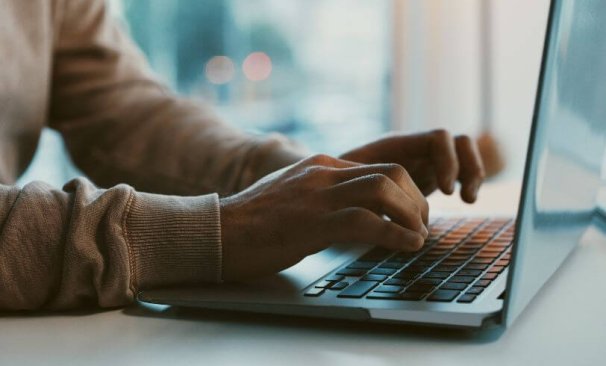 Na imagem há um notebook e mãos digitando no teclado.