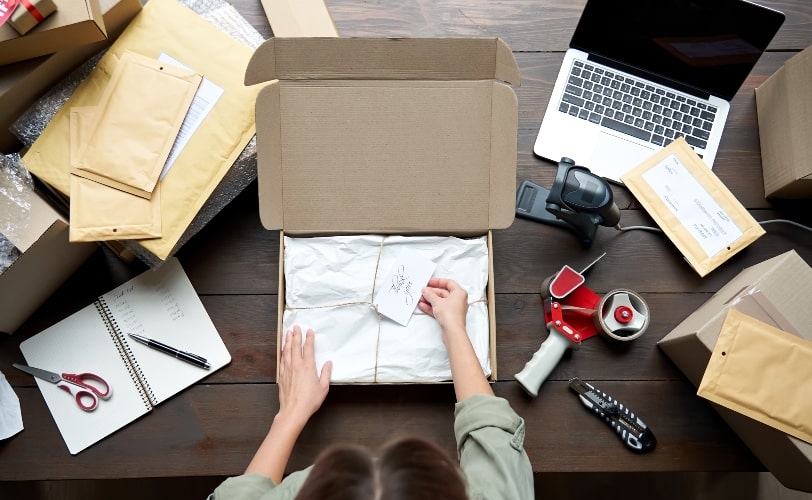 A imagem mostra uma mulher olhando uma caixa com um presente e faz referência a estratégia de merchandising e como passar informações a potenciais clientes.