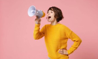 a imagem mostra uma mulher frente a uma parede rosa com um megafone. A imagem faz referência a personificação de marca.