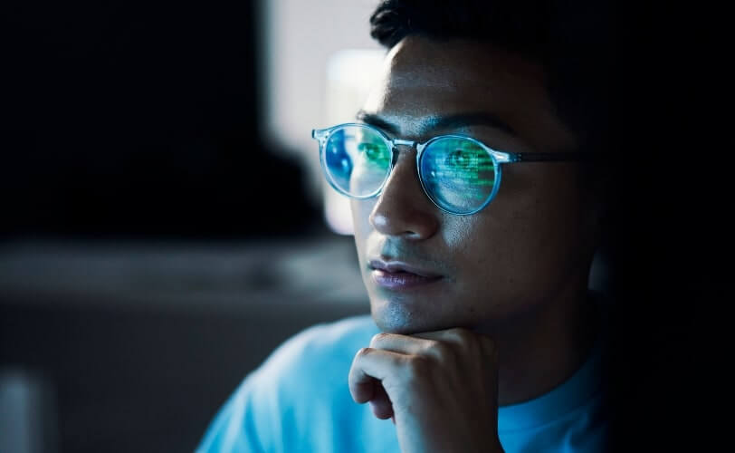 A imagem mostra um homem olhando para uma tela de computador. Ele está programando com o cURL, por isso é possível ver alguns códigos refletidos na cor verde nas lentes de seus óculos.