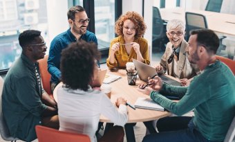 Na imagem pessoas estão ao sentados a uma mesa e estão conversando felizes.