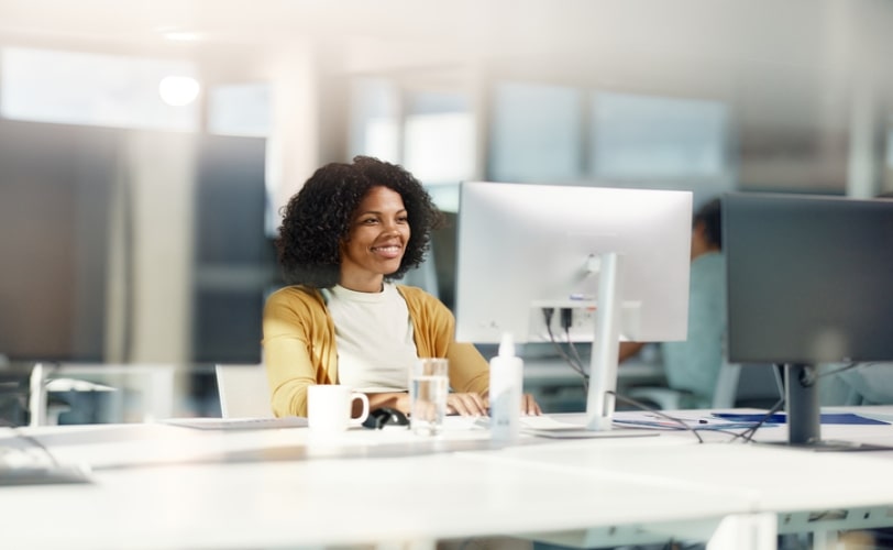 mulher sorridente frende a uma tela de computador em um escritório corporativo.