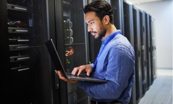 Homem com laptop em frente a um servidor para manutenção, segurança cibernética e verificação de internet.