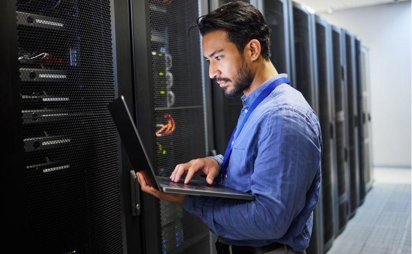 Homem com laptop em frente a um servidor para manutenção, segurança cibernética e verificação de internet.