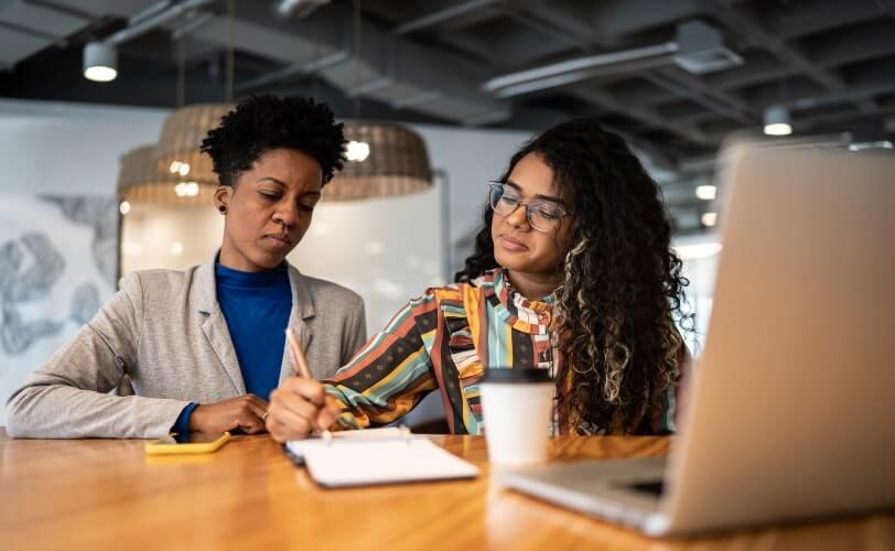 Duas mulheres sentadas frente a uma mesa de escritório.