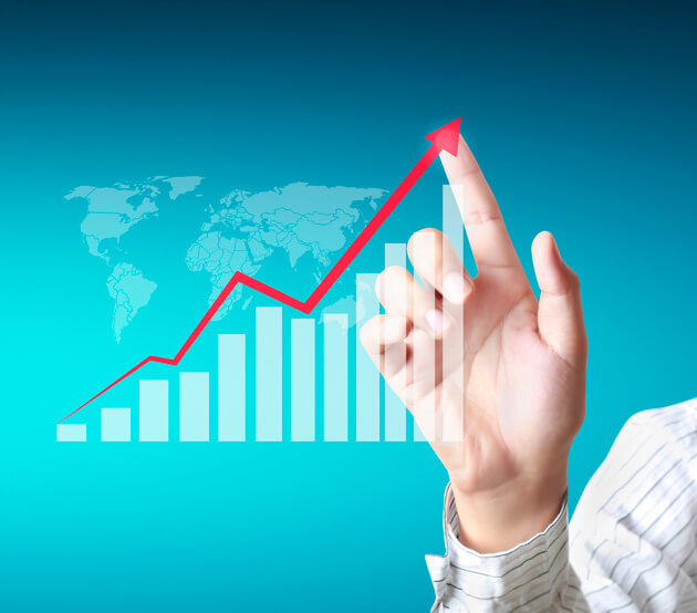 Uma mão aponta para uma linha vermelha com tendência ascendente em um gráfico financeiro do tipo tabela. O fundo da imagem é  azul claro e tem  um mapa-múndi tênue por trás dos dados. A imagem representa crescimento ou sucesso nos negócios ou finanças.