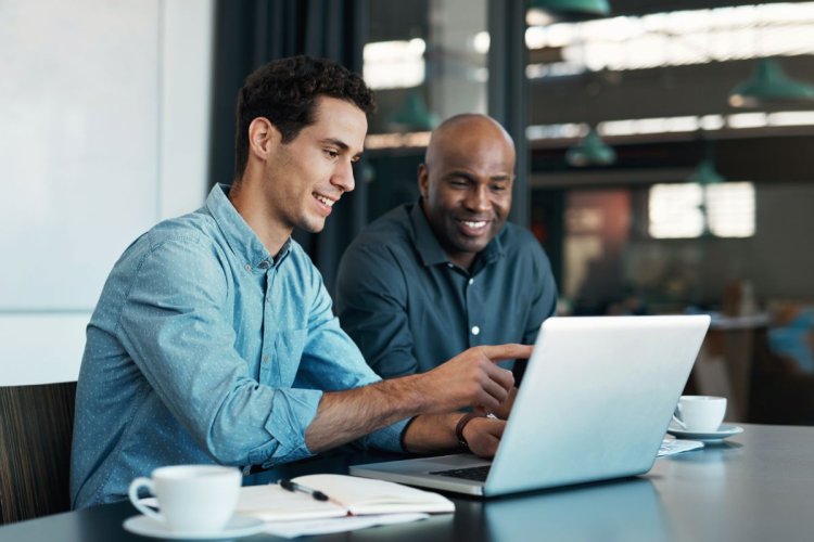 A imagem mostra dois homens conversando em um escritório. Um deles está apontando para a tela do notebook, mostrando um site criado para ajudar a empresa a conquistar uma presença digital ainda maior.