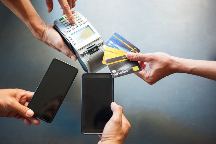 Mãos segurando um cartão de crédito próximo a uma máquina de cartão, simbolizando transações financeiras distintas.