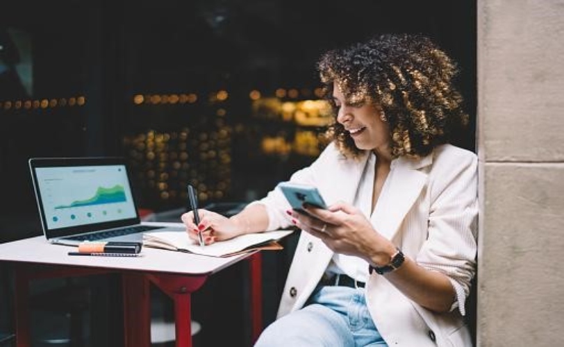 Mulher mexendo no celular e fazendo anotações