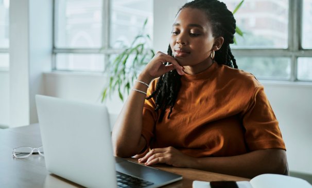 A imagem mostra uma mulher negra em um escritório com uma expressão pensativa. Ela está avaliando como aplicar os recursos da CDN para melhorar o desempenho do site de sua empresa.