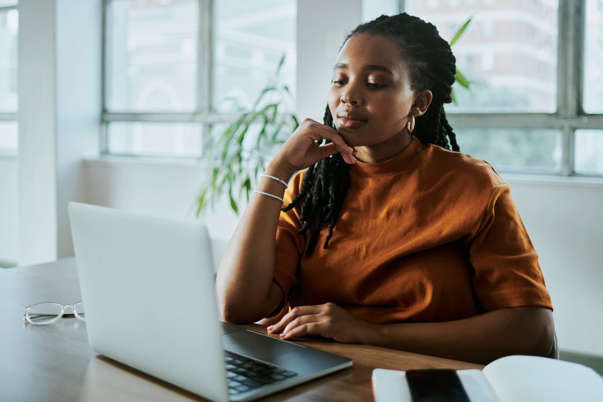 A imagem mostra uma mulher negra em um escritório com uma expressão pensativa. Ela está avaliando como aplicar os recursos da CDN para melhorar o desempenho do site de sua empresa.