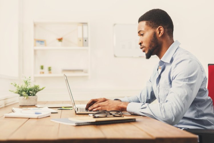 A imagem mostra um homem negro trabalhando em seu computador em casa. Ele está concentrando, analisando como o uso da VPS e a otimização de sites, em conjunto com a CDN, pode entregar o melhor conteúdo.