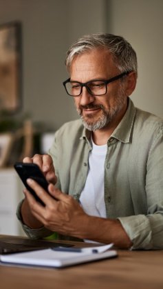 A imagem mostra um homem de meia-idade diante de um notebook e com um celular na mão. Após alguns trabalhos com localhost, ele verifica o funcionamento de uma aplicação no smartphone.