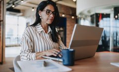 A imagem mostra uma mulher de meia-idade usando roupa social em um escritório. Ela está diante de um notebook, trabalhando na construção de sites e otimizando imagens WebP para deixá-los mais rápidos.