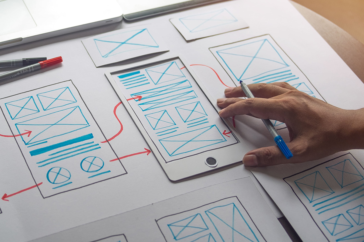 Designer gráfico trabalhando em um projeto responsivo. Ele está criando um esboço inicial para definir a estrutura e o layout da interface.