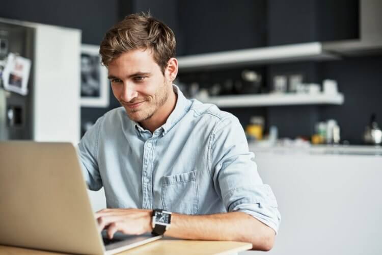 A imagem mostra um homem jovem no que parece ser a cozinha de um escritório com um notebook sobre a mesa. Ele está usando o dispositivo para acessar arquivos enviados por meio de um cliente FTP.