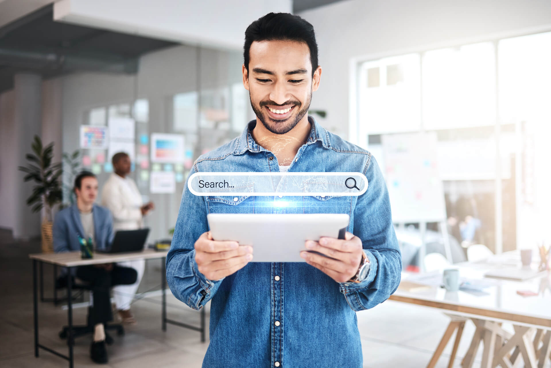 Homem branco em um escritório, vestido com camisa jeans, utilizando um tablet com interface holográfica de um motor de busca personalizado.