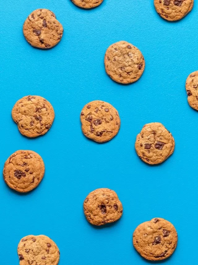 A imagem apresenta um fundo azul-claro e vários cookies com gotas de chocolate enfileirados, um ao lado do outro, além de outros posicionados em cima, embaixo e nas diagonais.