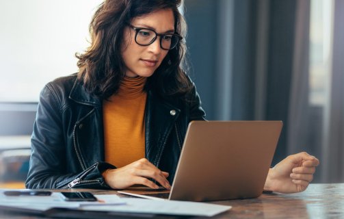 A imagem mostra uma mulher digitando em um notebook, provavelmente em um escritório. Ela está fazendo uma pesquisa para obter informações sobre FQDN, já que ele é importante para o funcionamento de uma rede.