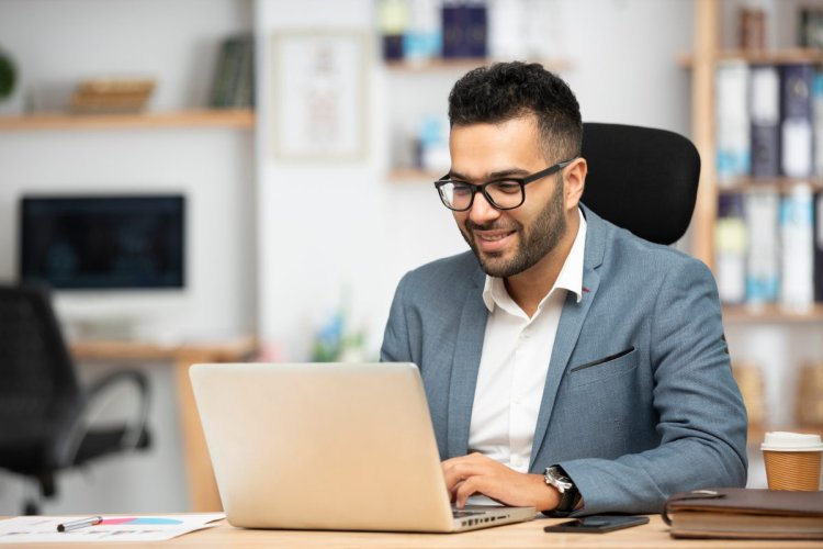 A imagem mostra um homem vestindo roupa social em um escritório. Ele está digitando em um notebook para acessar um site que provavelmente foi configurado com auxílio de um FQDN. 