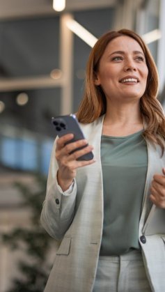 A imagem mostra uma mulher com roupa social no que parece ser o saguão de um escritório. Ela segura o celular em uma mão e uma pasta na outra, olhando para o horizonte enquanto pensa em formas de como monetizar no Instagram.