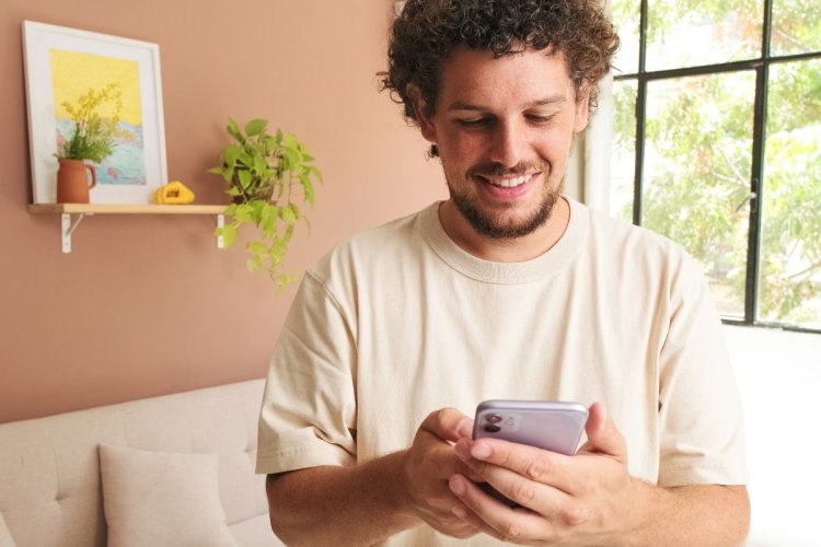 A imagem mostra um homem sentado no chão de uma sala de estar. Ele está sorrindo enquanto olha para tela, o que significa que a estratégia de como monetizar no Instagram adotada pela empresa dona do perfil está surtindo efeito. 