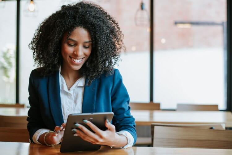 A imagem mostra uma mulher de roupas sociais segurando um tablet. Ela está em um escritório, possivelmente usando o seu tempo livre para acessar um site seguro, que conta com protocolo HTTPS.