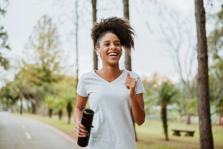 A imagem mostra uma mulher correndo ao ar livre em um parque. Ela segura uma garrafa de água, um item que está na lista dos produtos mais vendidos na internet. 