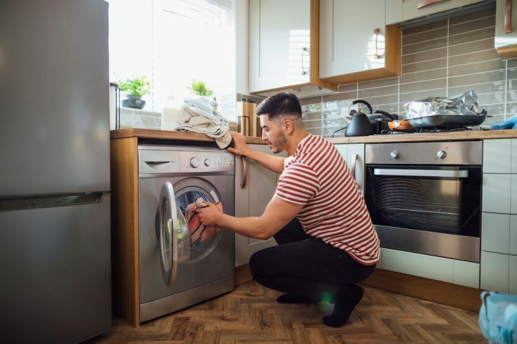 A imagem mostra um homem utilizando uma máquina de lavar na cozinha de casa. Por conta das buscas, o setor de eletrodomésticos é um dos mais interessantes para quem quer vender e comprar na internet. 