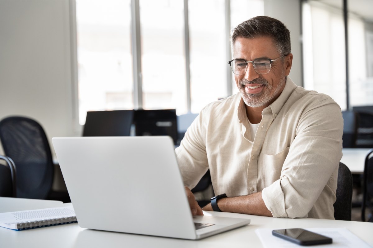 A imagem mostra um homem de meia-idade em um escritório digitando em um notebook. Ele possivelmente está analisando um slug que foi criado para a publicação de um post em seu blog.