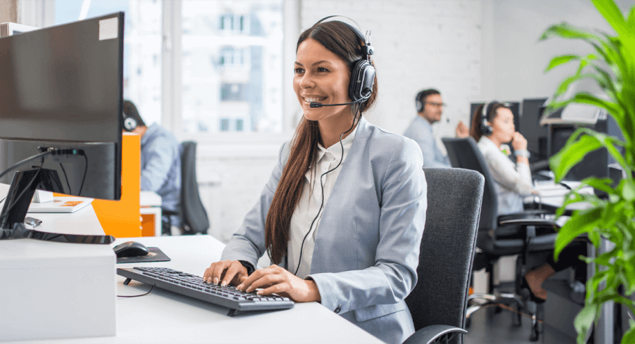 Mulher sorridente usando fone de ouvido, trabalhando em um ambiente de atendimento ao cliente ou call center, com um colega ao fundo.
Legenda: Empatia no atendimento transforma relações! Coloque-se no lugar do cliente e faça a diferença com um serviço humano e ágil.
