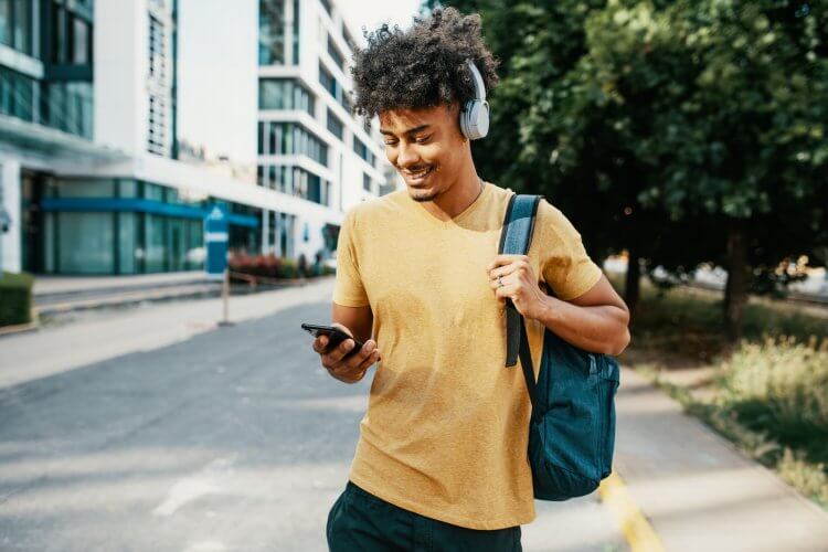 A imagem mostra um rapaz negro andando na calçada enquanto checa um smartphone. Ele carrega em um dos ombros uma mochila, possivelmente indo para a escola ou para a faculdade. No caminho, ele foi impactado pela mensagem de uma empresa que analisou os melhores horários para publicar no Instagram. 