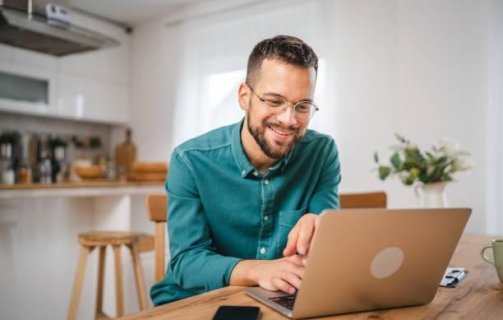 A imagem mostra um homem trabalhando em um notebook. Ele está no que parece ser a cozinha de um escritório e, possivelmente, está realizando uma busca para saber como descobrir a fonte de uma imagem na internet.