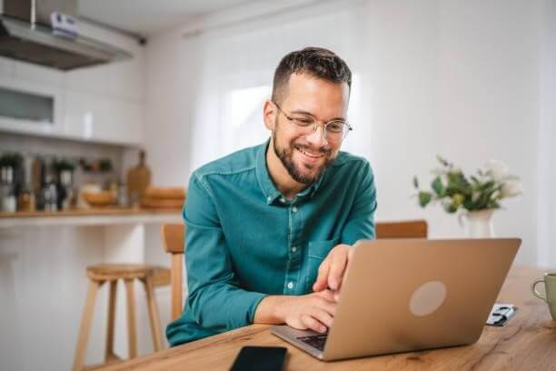 A imagem mostra um homem trabalhando em um notebook. Ele está no que parece ser a cozinha de um escritório e, possivelmente, está realizando uma busca para saber como descobrir a fonte de uma imagem na internet.